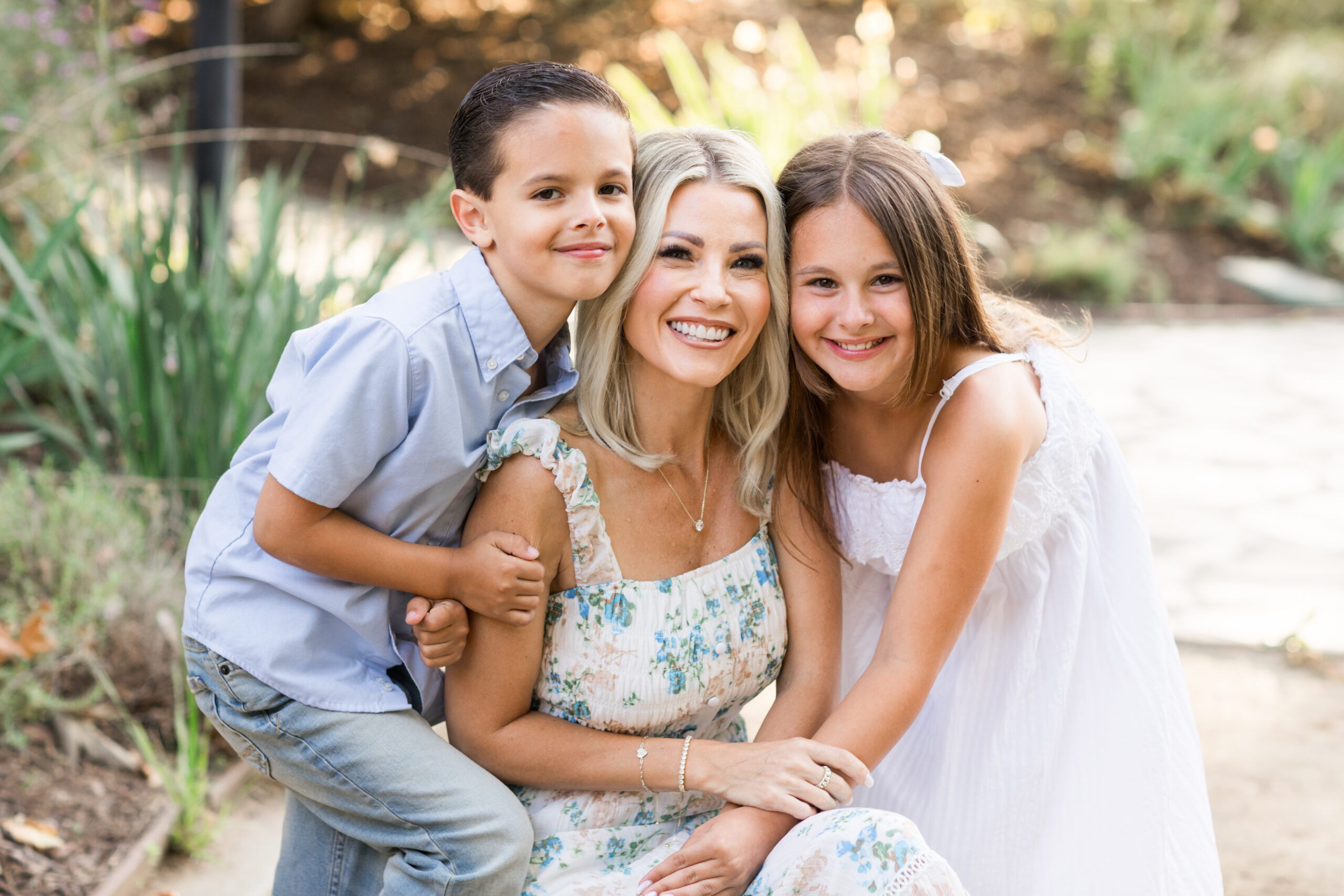 A beautiful blonde mother sitting between her son and daughter, cheek to cheek, smiling at the camera.
